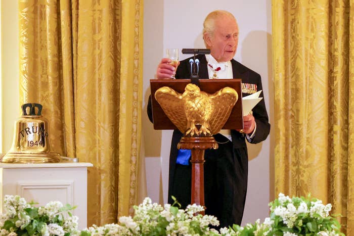 An older man  successful  ceremonial  attire with medals speaks astatine  a lectern with an eagle emblem, holding a solid  and notes, surrounded by a floral arrangement