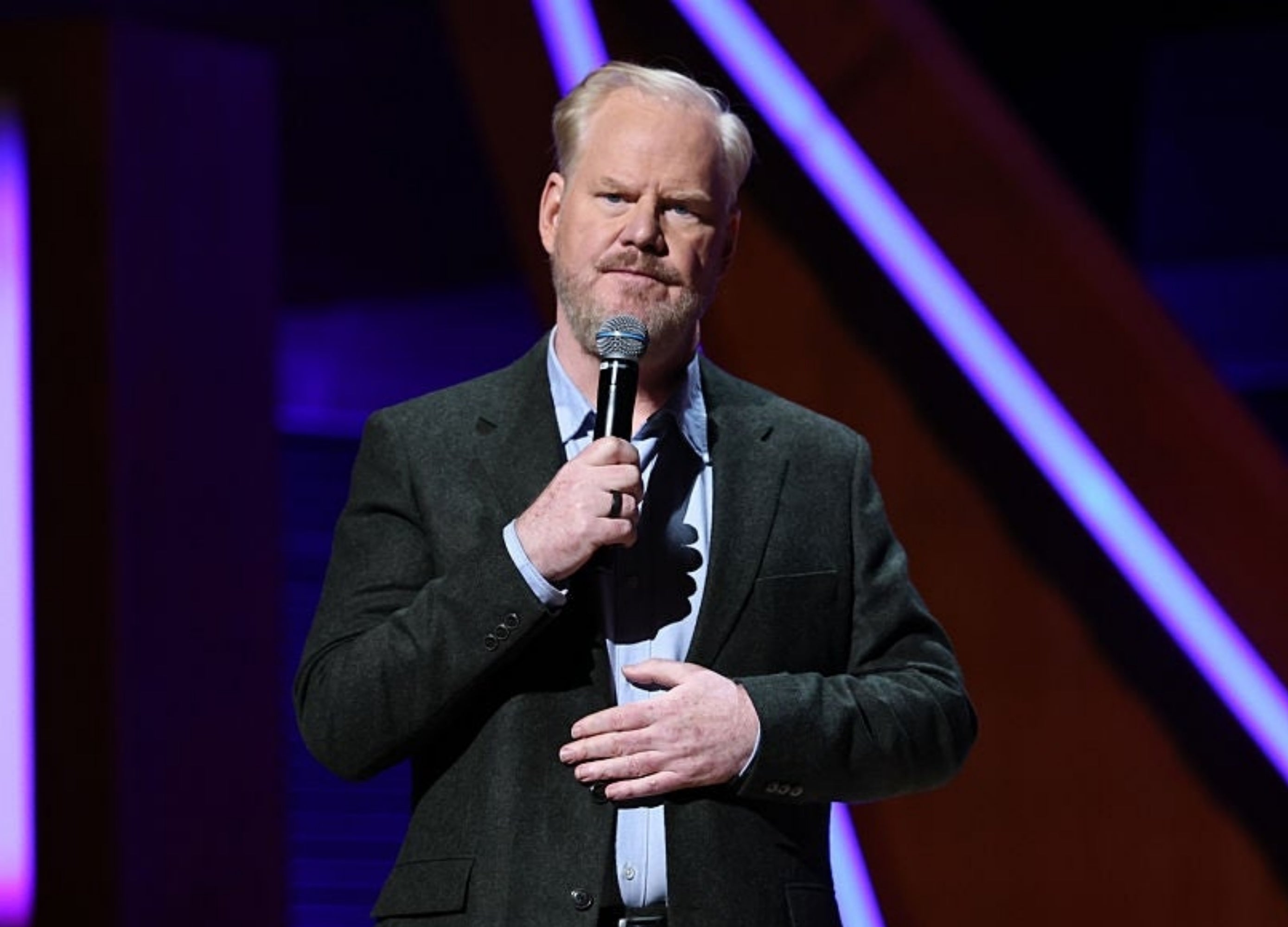 Person connected  signifier    holding a microphone, wearing a suit, performing stand-up comedy