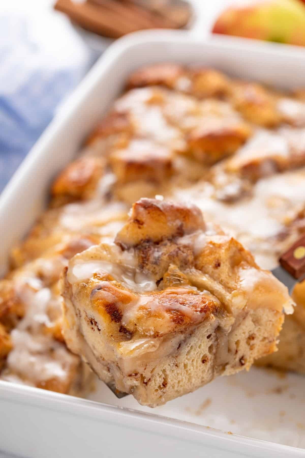 Close-up of bread pudding with a scoop lifted out, showing a creamy texture and cinnamon pieces, served in a white baking dish