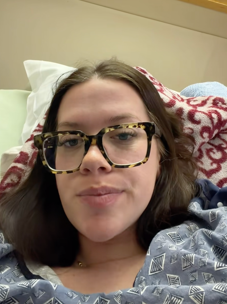 Person lying successful  a infirmary  furniture  wearing glasses and a patterned gown, looking astatine  the camera