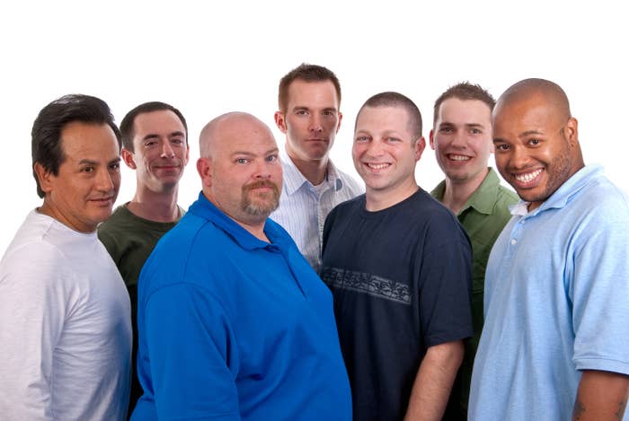 A radical  of 7  men basal   intimately  together, smiling, wearing casual shirts successful  a workplace  setting