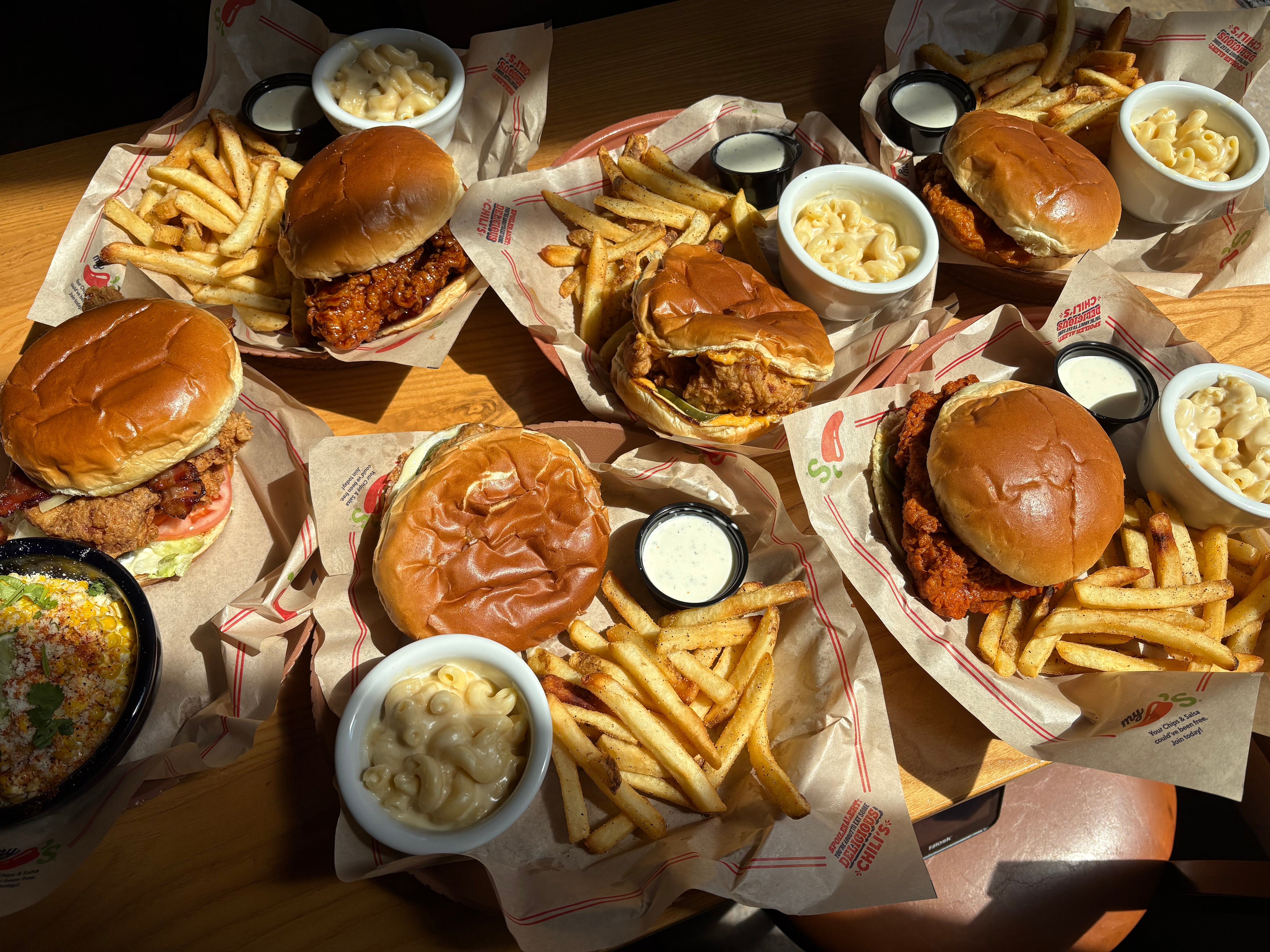 Plates of burgers, fries, mac and cheese, and creamy dipping sauce are set on a table, showcasing a hearty meal