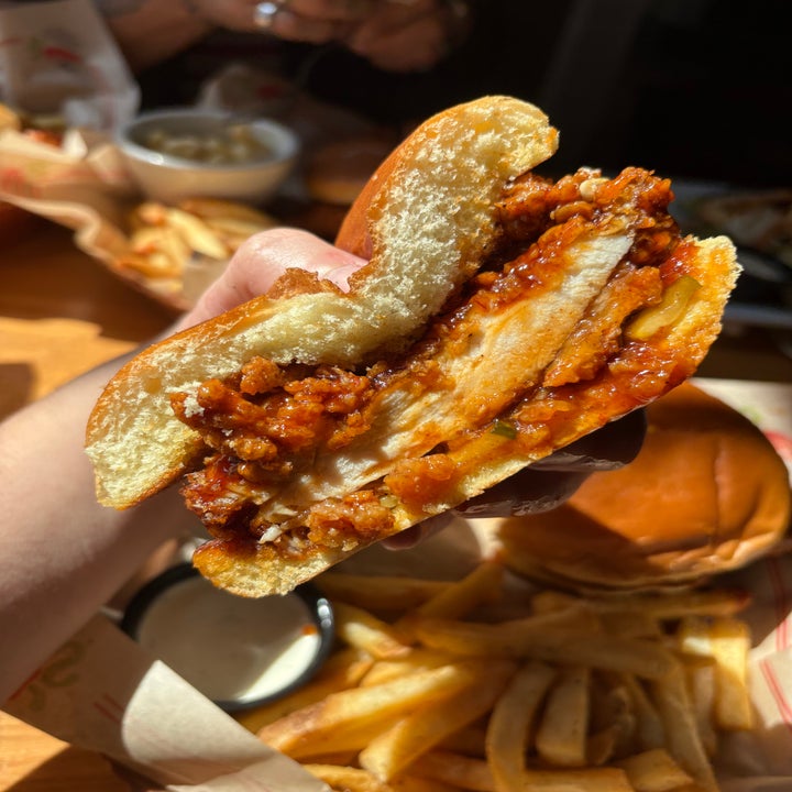 Close-up of a half-eaten crispy chicken sandwich held in hand, with fries in the background