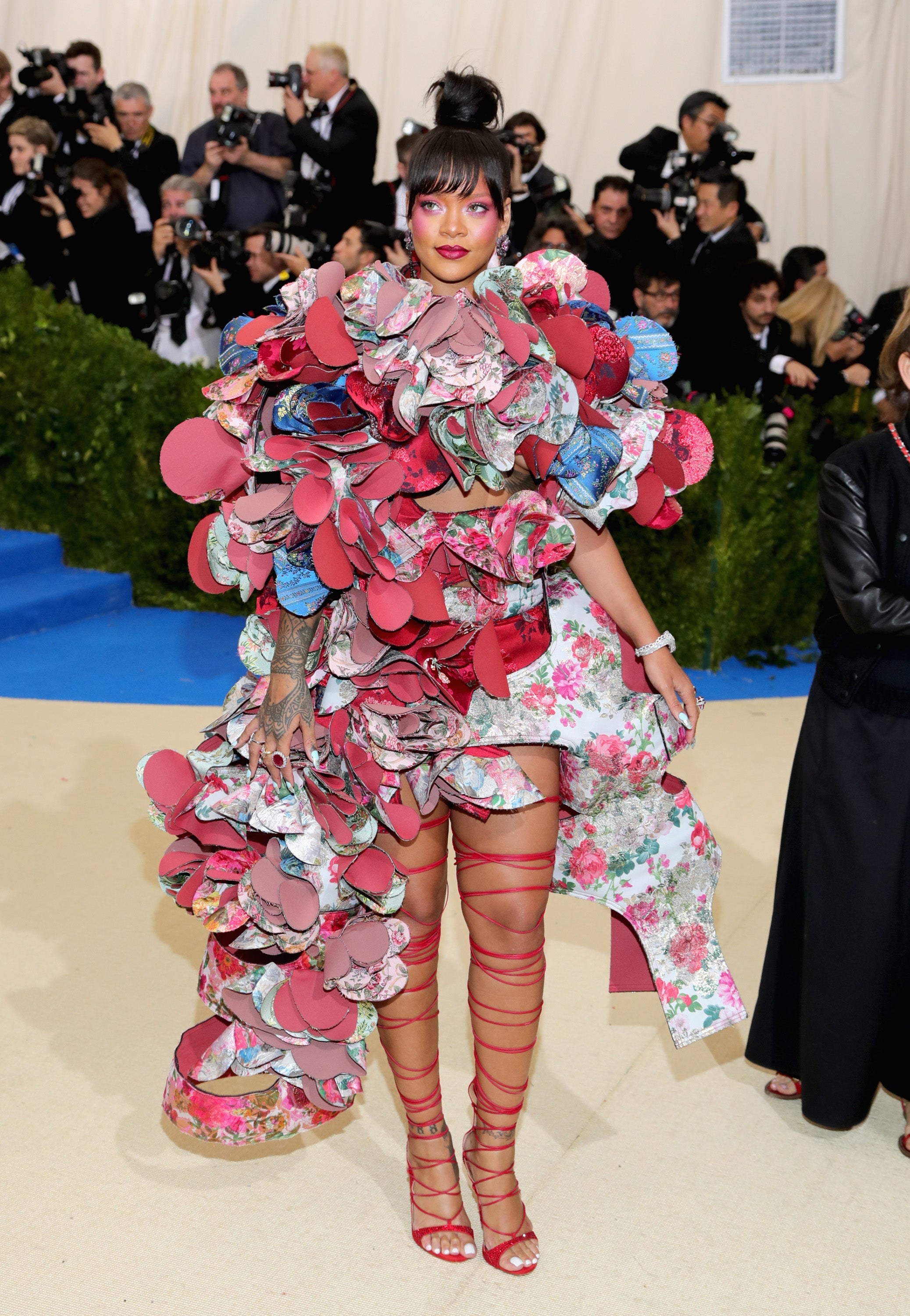 Person wearing an extravagant, floral-themed outfit with layered, sculptural details astatine  a ceremonial  event, surrounded by photographers