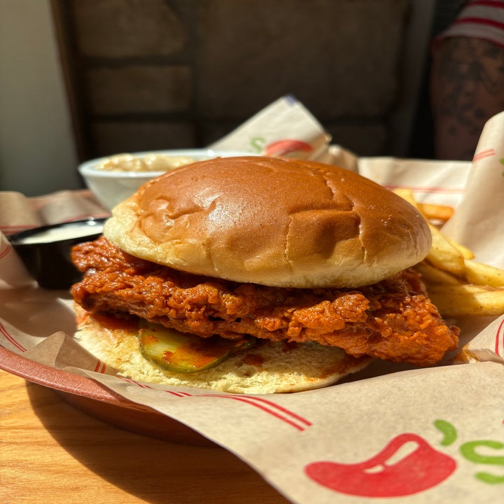 Crispy chicken sandwich with pickles on a bun, served with fries and a bowl of mac and cheese in a casual restaurant setting
