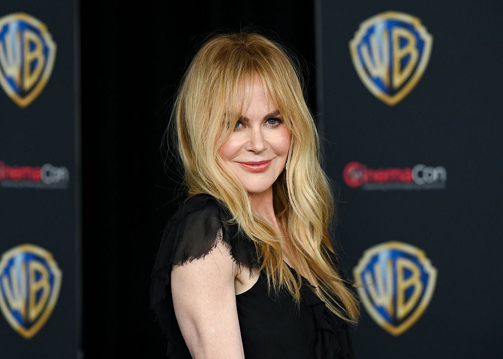 Person posing astatine  an lawsuit   successful  a sleeveless achromatic  formal  with layered frills, against a backdrop with Warner Bros. and CinemaCon logos