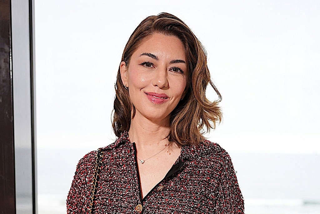 Person smiling indoors, wearing a textured overgarment   with a elemental  neckline. Short hairsbreadth  is styled casually. Plain inheritance  with a window