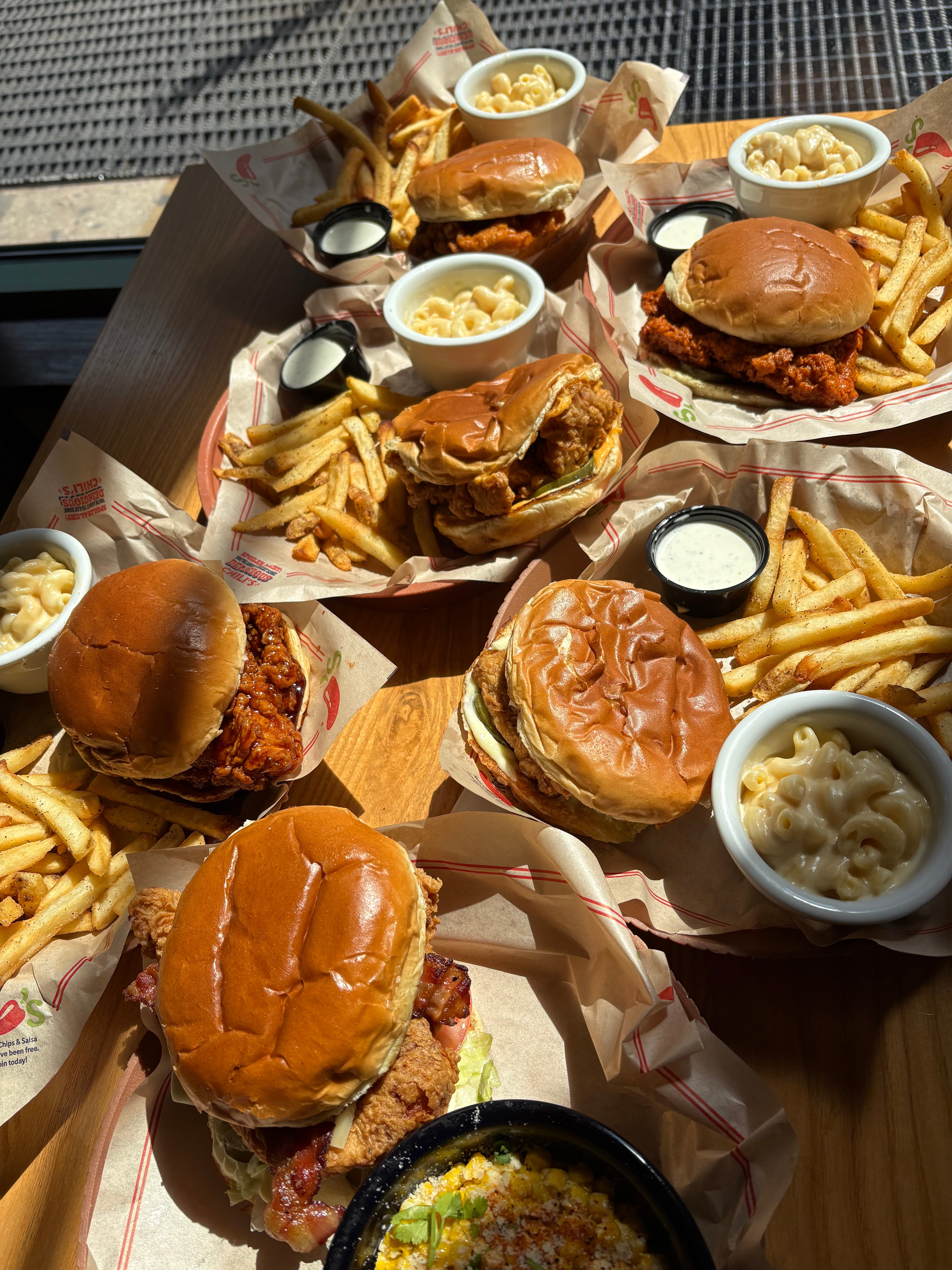 Four plates of burgers with fries and sides of mac and cheese and coleslaw on a wooden table at a restaurant