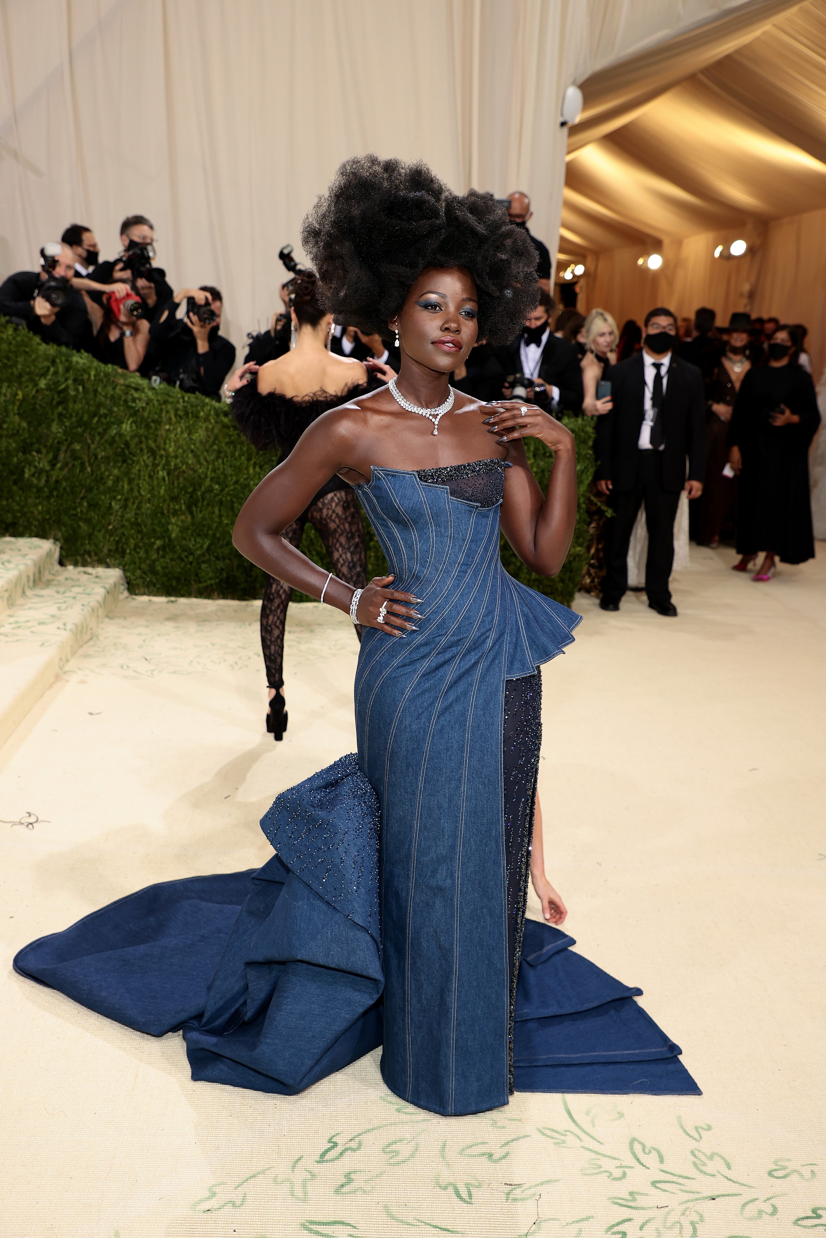 Person successful  a structured, layered denim gown with an elaborate hairstyle connected  a glamorous event's beige carpet. Photographers successful  the background