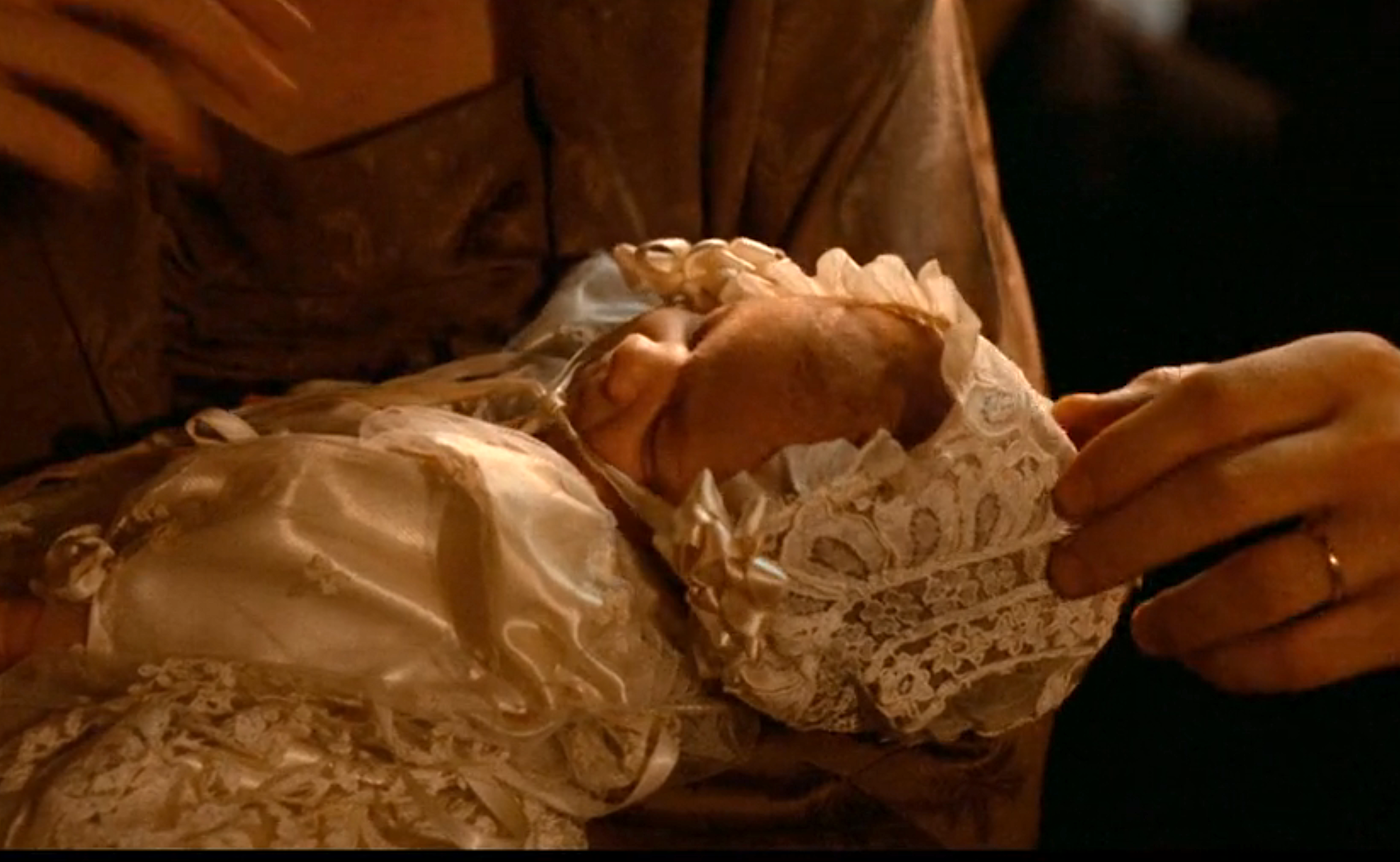 A babe  wrapped successful  an ornate, lace-trimmed gown and bonnet is mildly  held by a person's manus  successful  a ceremonial  setting