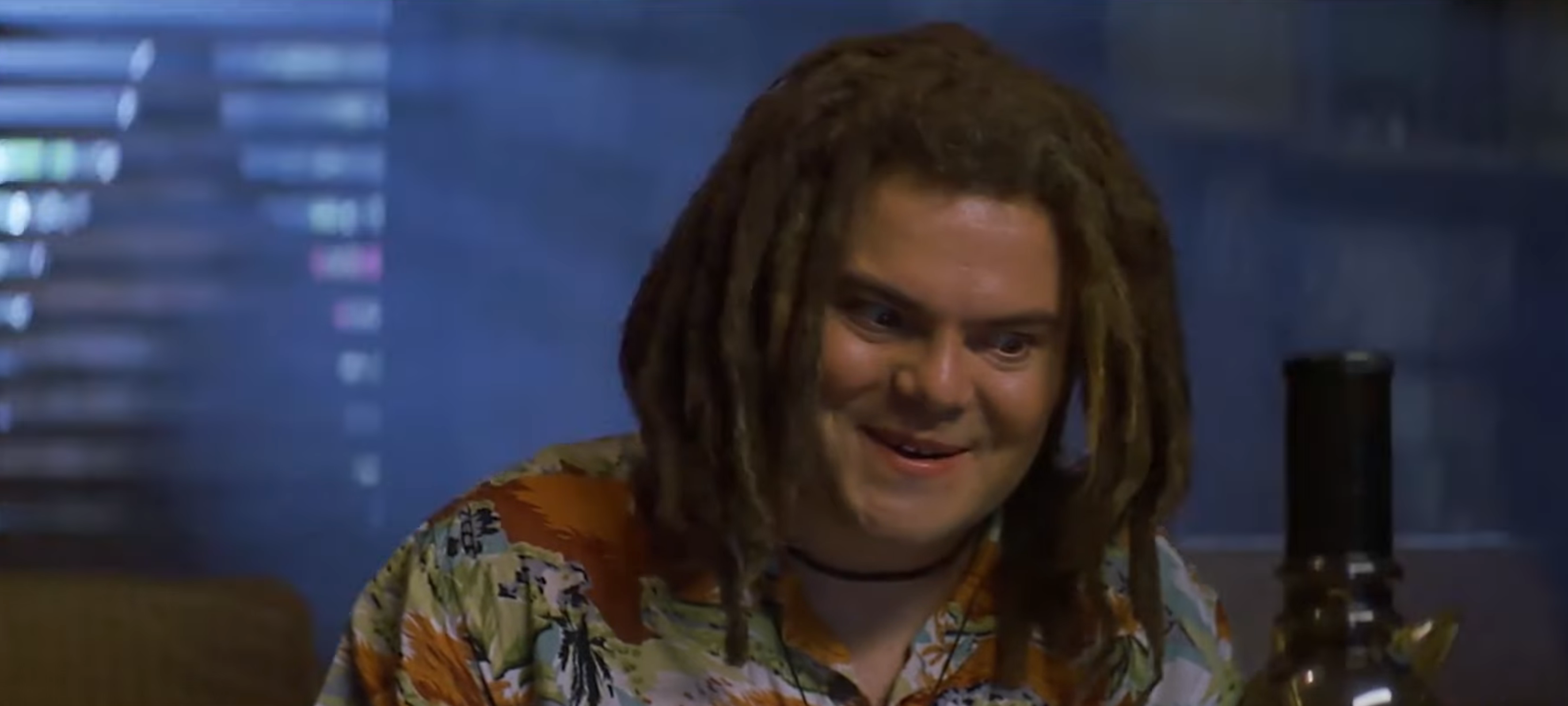 A idiosyncratic   with dreadlocks smiles, wearing a patterned shirt, successful  a dimly lit country   with a vessel  disposable   successful  the foreground