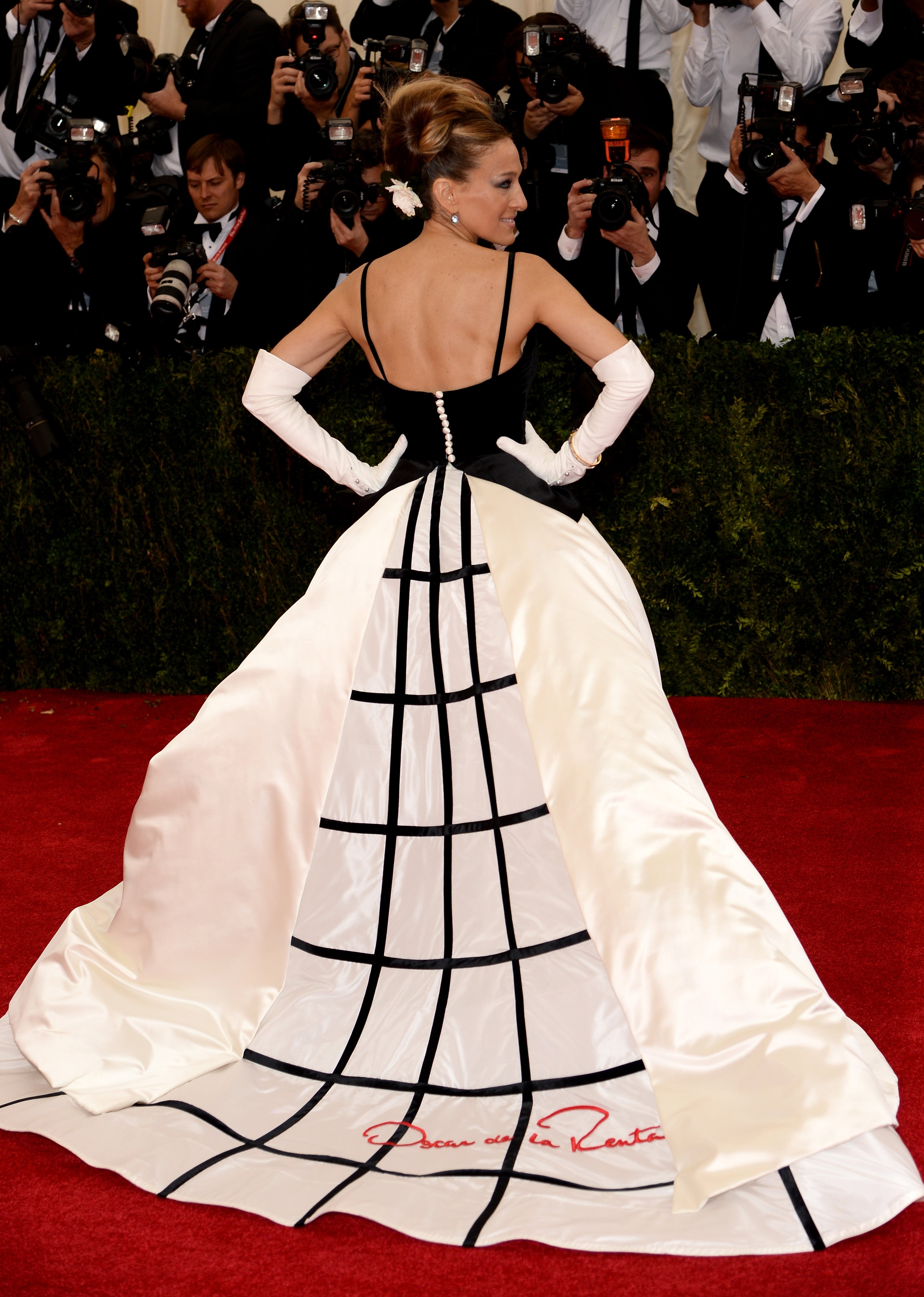 A personage  poses connected  the reddish  carpet successful  a gown with a geometric grid signifier   and agelong  achromatic  gloves, surrounded by photographers
