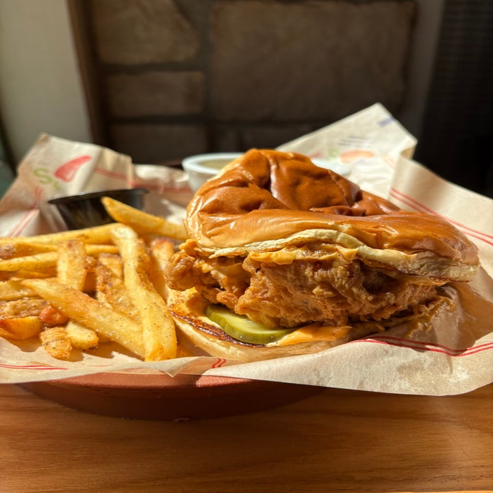 Fried chicken sandwich sandwich with pickles and seasoned fries on a tray, viewed in a casual dining setting