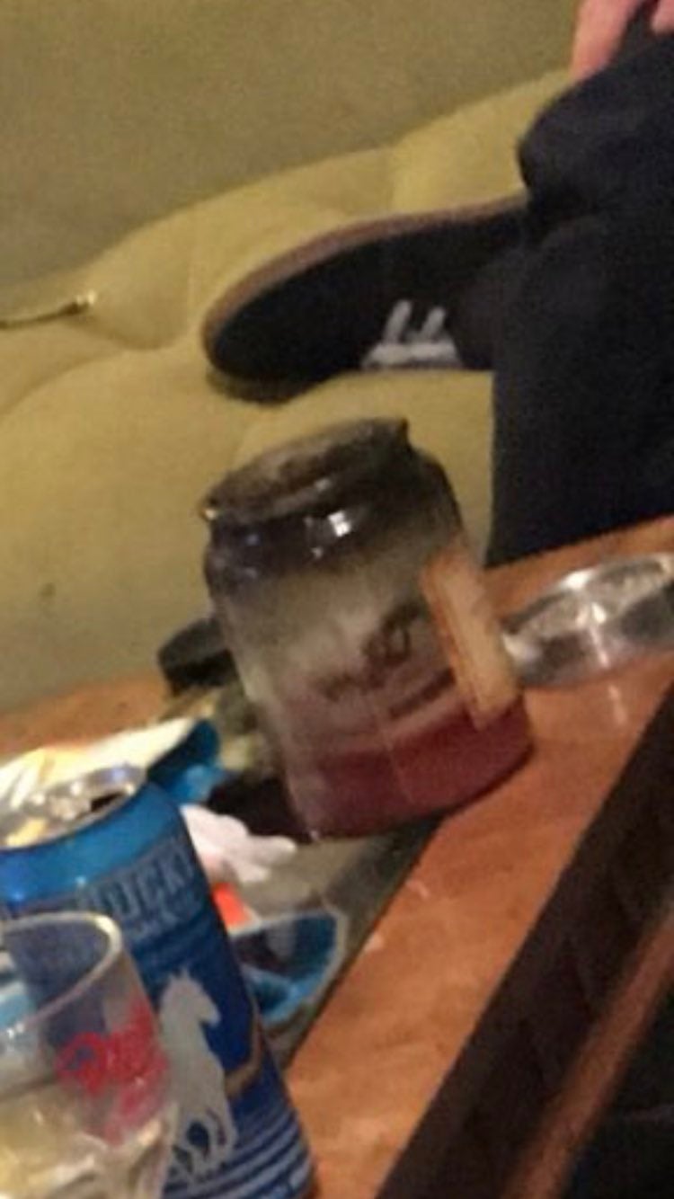 Jar filled with reddish  liquid connected  a java  table, surrounded by a tin  and a glass, adjacent  to a idiosyncratic   sitting connected  a couch