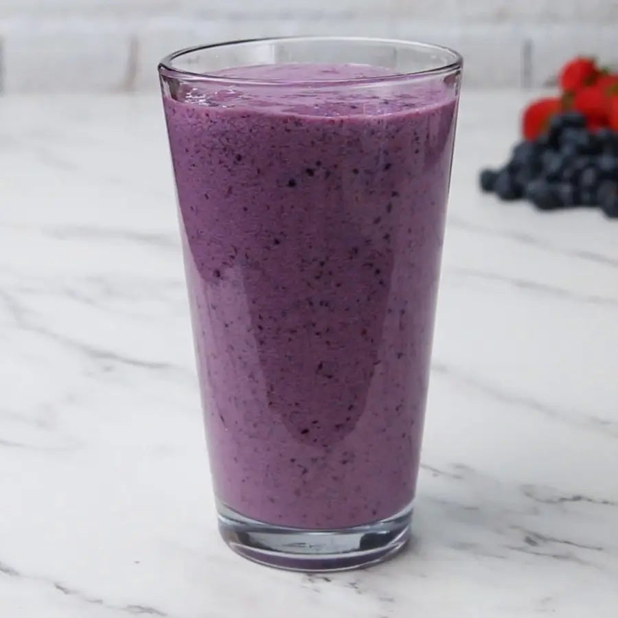 Glass of berry smoothie on a marble countertop, with blueberries and strawberries in the background