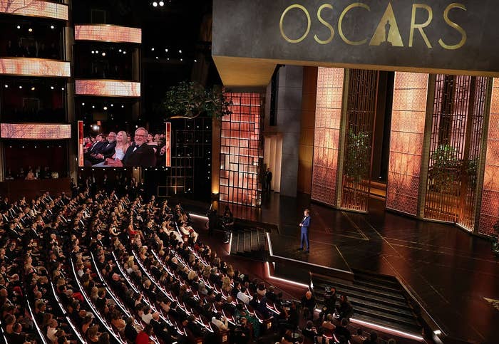 A wide   presumption    of an Oscars ceremony, featuring a filled auditorium and a big   speaking connected  signifier    beneath   a ample  "Oscars" sign