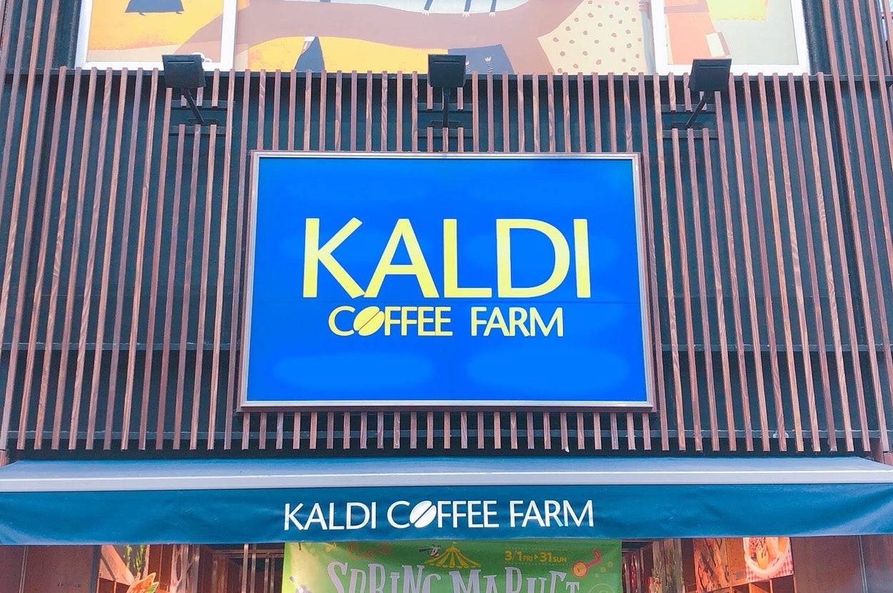 カルディコーヒーファーム店の外観。青い看板に黄色のロゴ。店舗名の下には「スプリングマーケット」の文字。