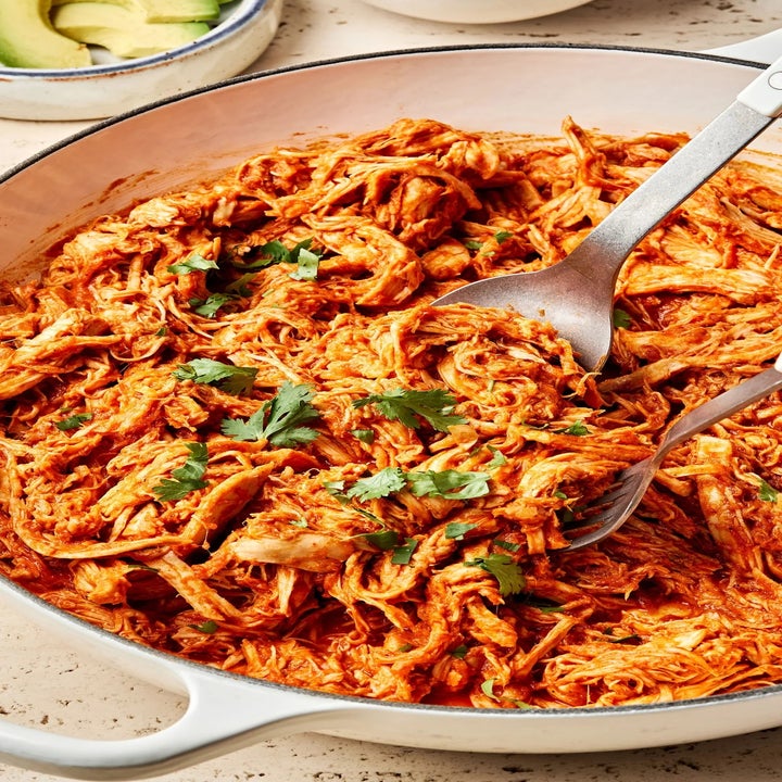 Shredded chicken in a skillet topped with cilantro, served with sliced avocado on the side