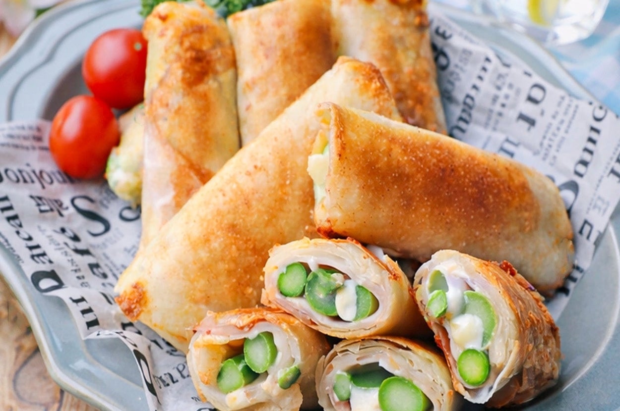 春巻きに似た料理。アスパラガスや他の具材が見えている。皿にはトマトと緑の野菜も添えられている。