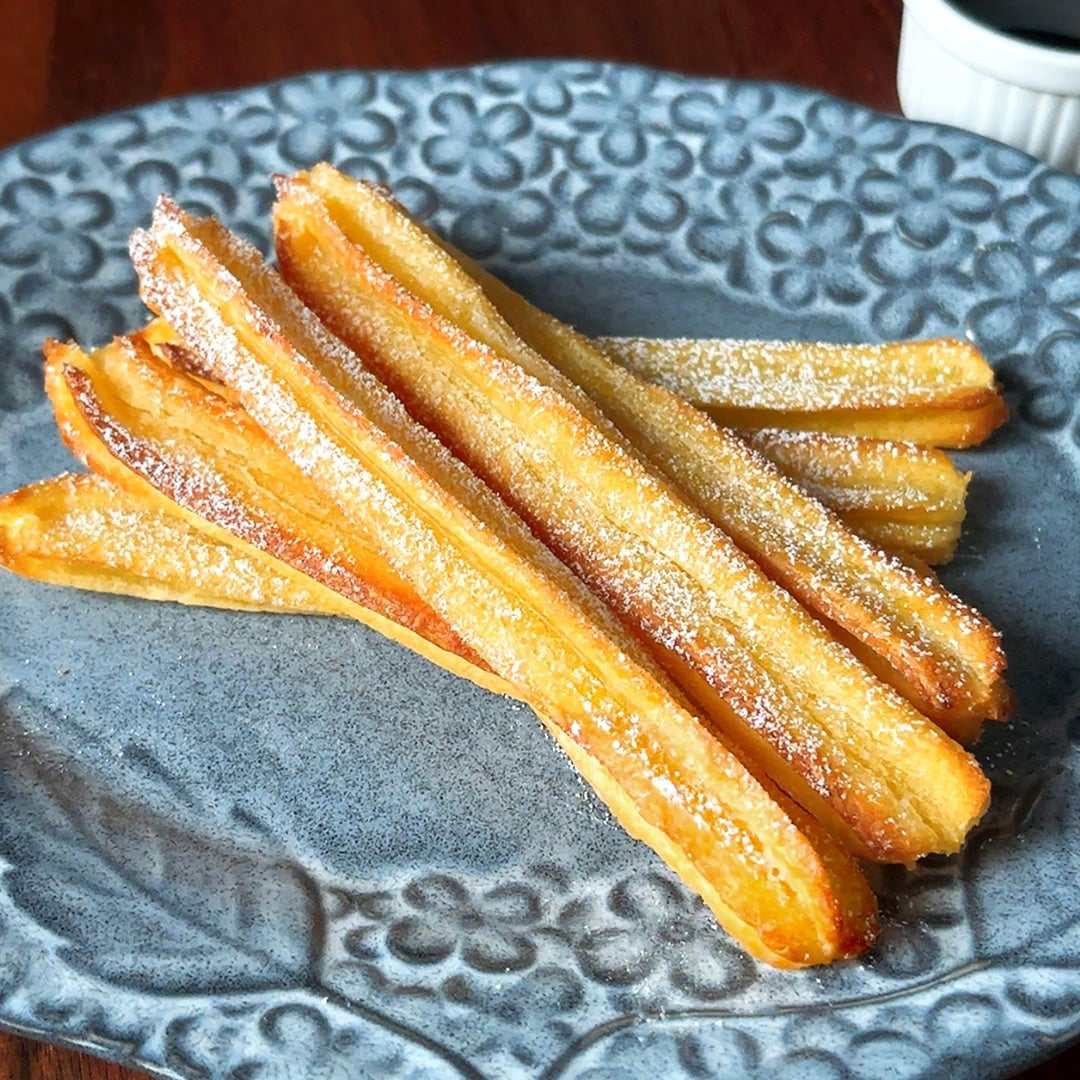 揚げたチュロスが皿に盛られている。砂糖がふりかけられ、おいしそうに見える。