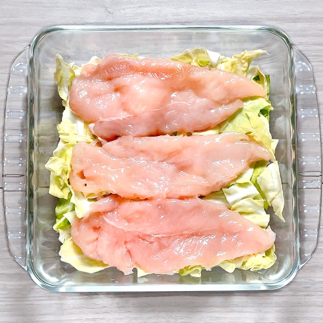 ガラスの容器にキャベツの上に置かれた生の鶏肉の切り身。