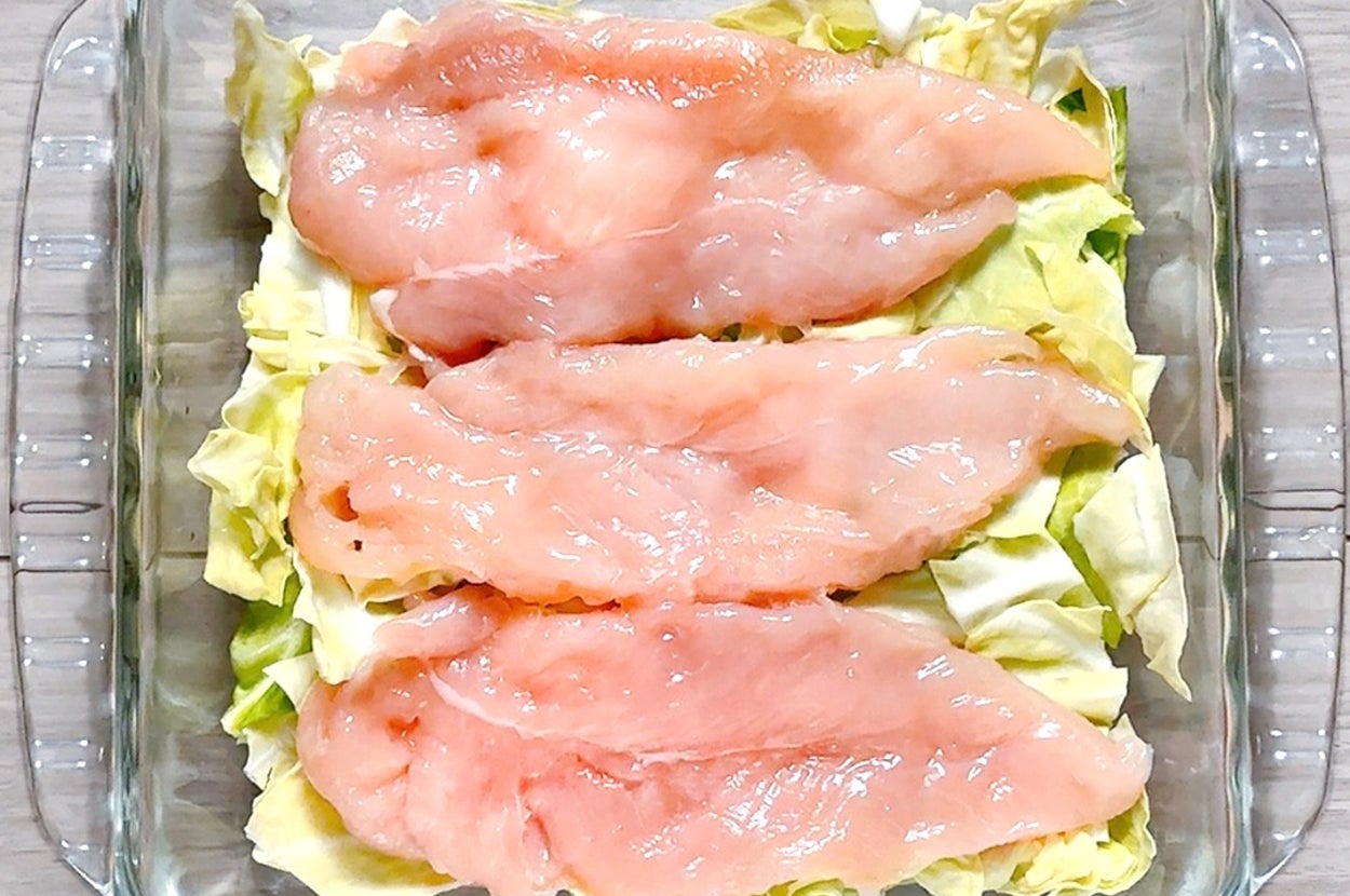 ガラスの容器にキャベツの上に置かれた生の鶏肉の切り身。