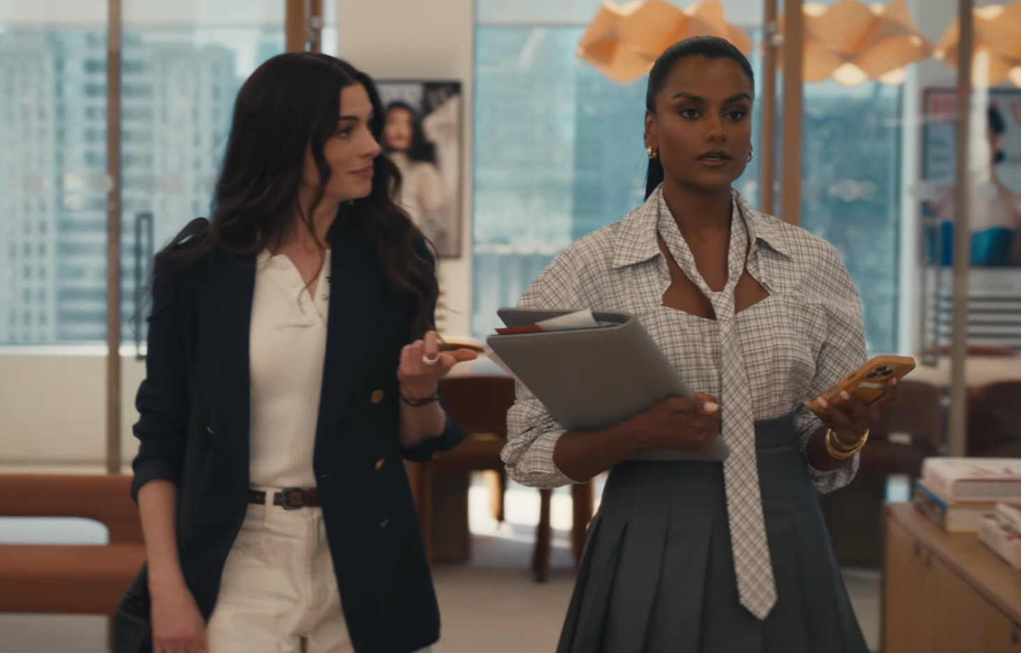 Two women successful  an bureau   setting; 1  wears a blazer and pants, the different   a blouse and skirt, holding documents and a phone
