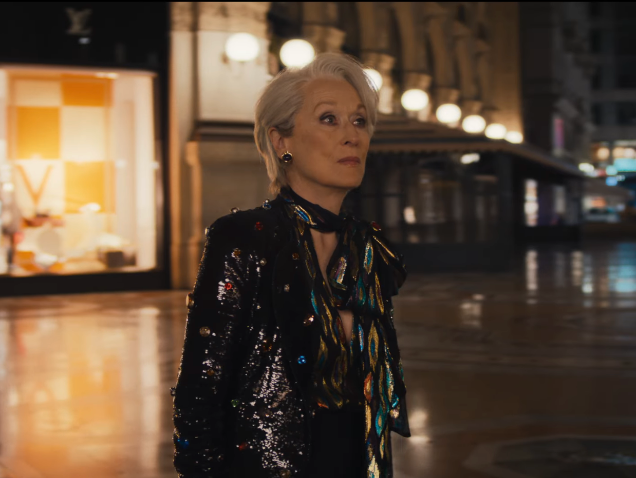 Person wearing a sequin overgarment   and patterned scarf, walking done  a dimly lit, elegant indoor mounting  with vintage decor