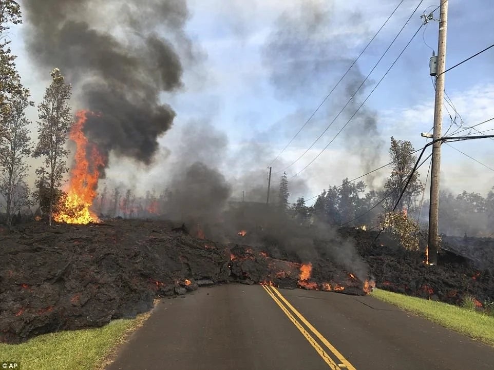 Lava travel  and fume  screen  a road, with flames rising, indicating volcanic enactment   successful  a forested area