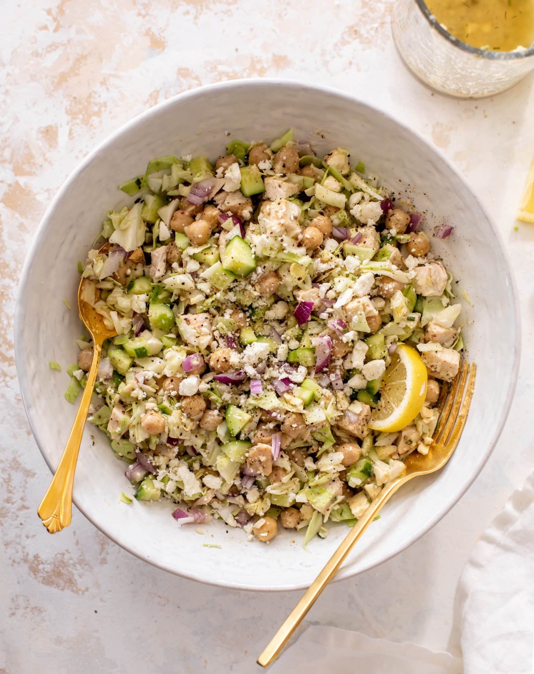 Chickpea and vegetable salad in a bowl with lemon wedge and two gold utensils