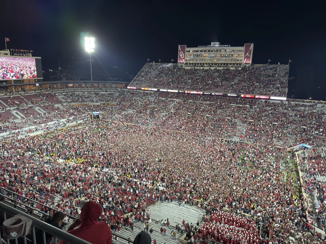 A packed shot   stadium with fans flooding the field, celebrating a game. Stadium lights illuminate the nighttime  scene