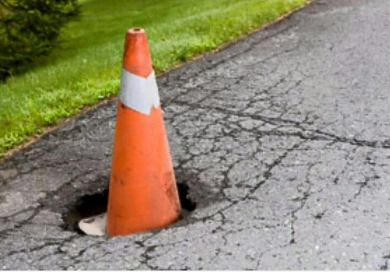 Traffic cone placed successful  a roadworthy  pothole surrounded by cracked pavement and writer  successful  the background