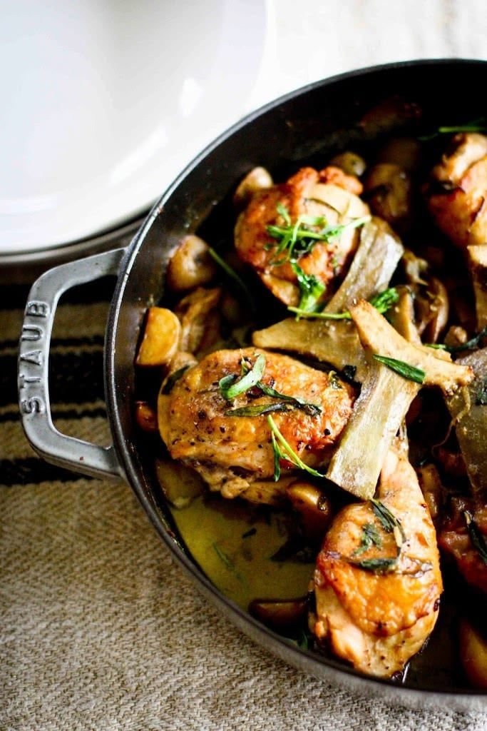 Dish of braised chicken with mushrooms and herbs in a cast-iron skillet on a table
