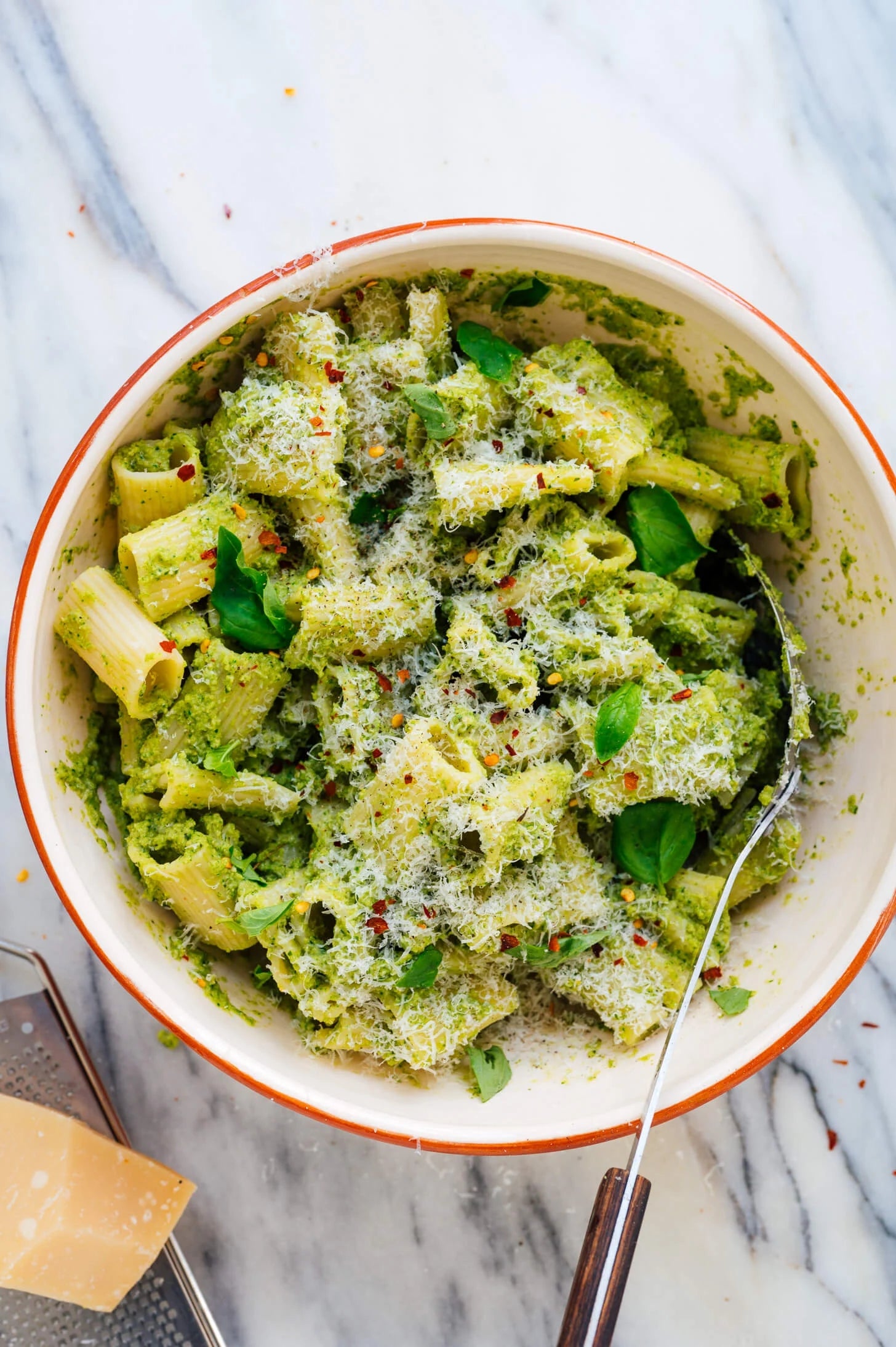 Bowl of rigatoni pasta tossed in creamy green pesto sauce, garnished with grated cheese and fresh basil leaves