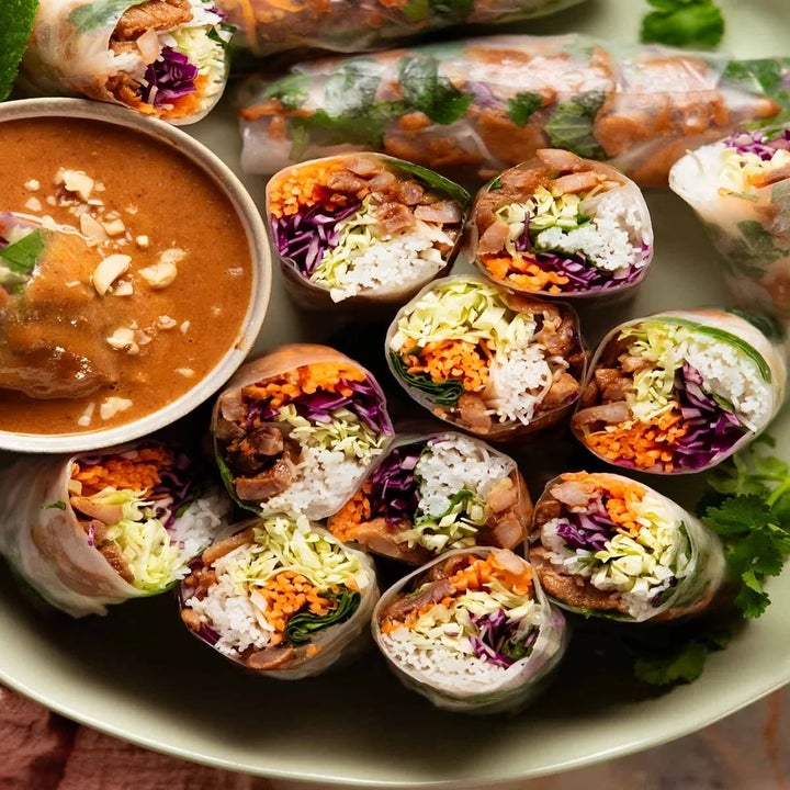 Plate of fresh spring rolls with colorful veggies and herbs, served with a side of peanut dipping sauce