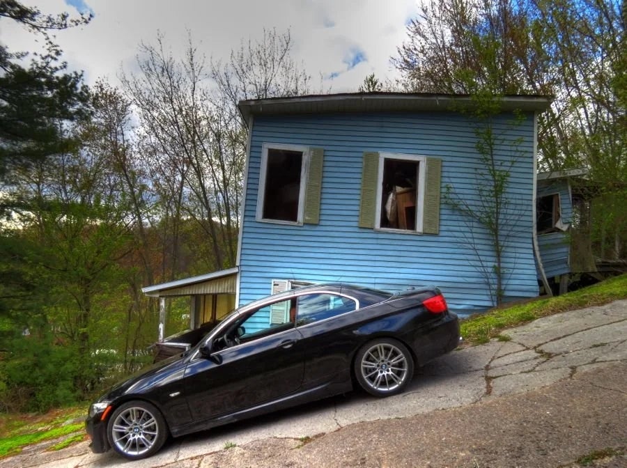 A achromatic  car   parked connected  a steep incline successful  beforehand   of a tilted, bluish  location   with unfastened  windows and trees around