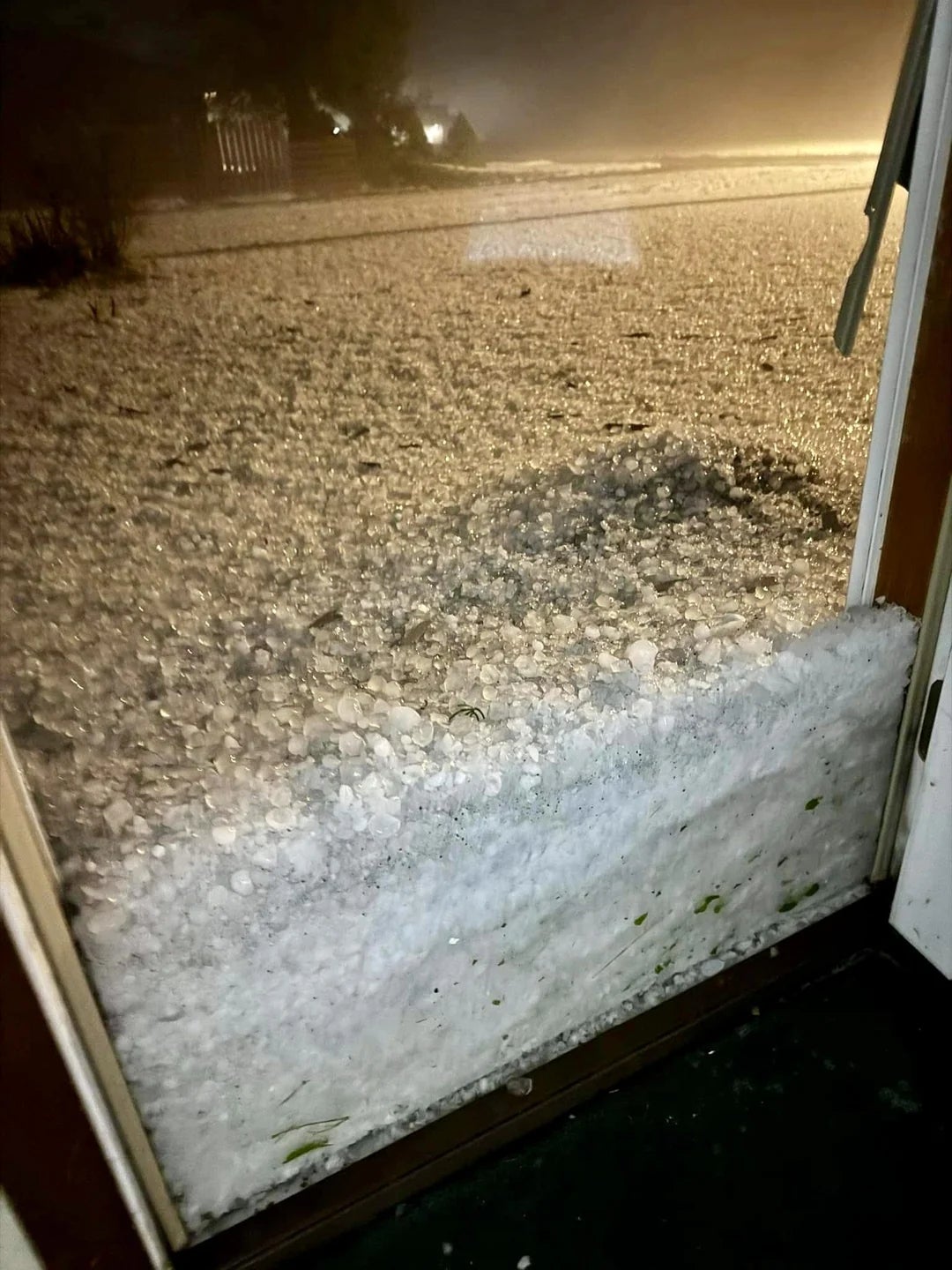 Large hailstones are piled against a solid  door, creating a heavy   icy barrier, indicating a caller    terrible  hailstorm outside