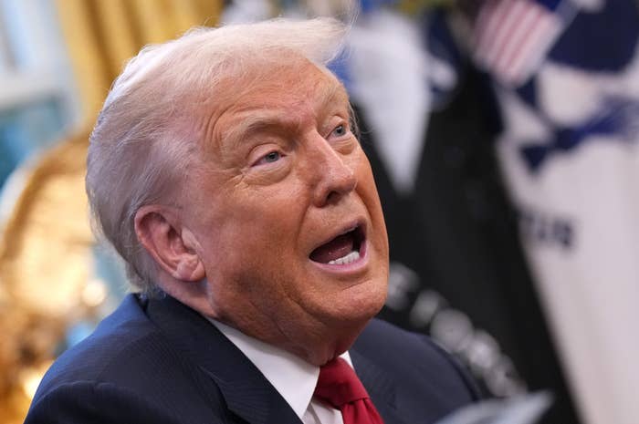 A idiosyncratic   successful  a suit   and necktie  is speaking with an expressive unfastened  mouth, indoors, with blurred flags successful  the background