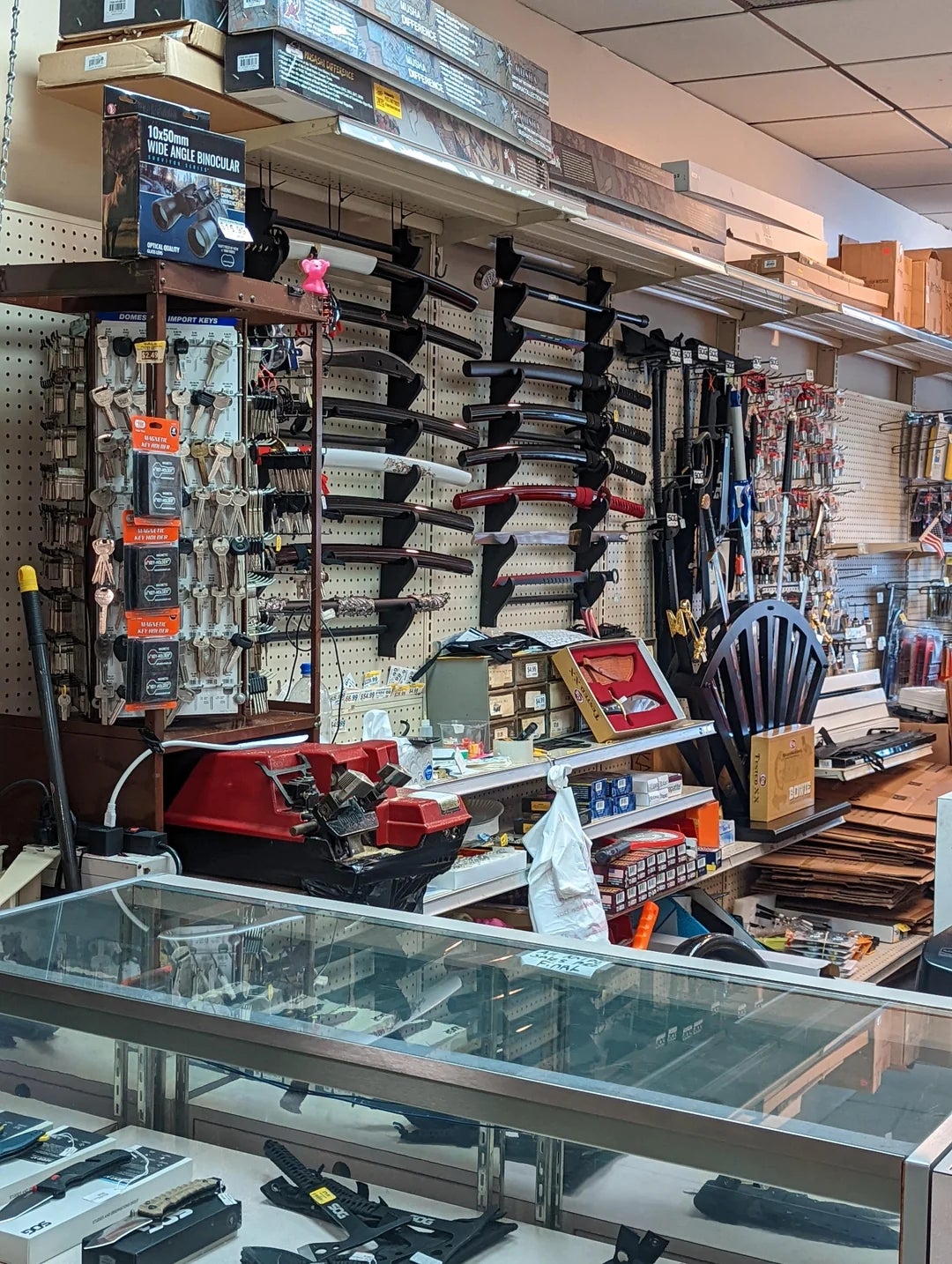 Hardware store   interior with shelves displaying tools, knives, and supplies; a solid  countertop showcases further  items