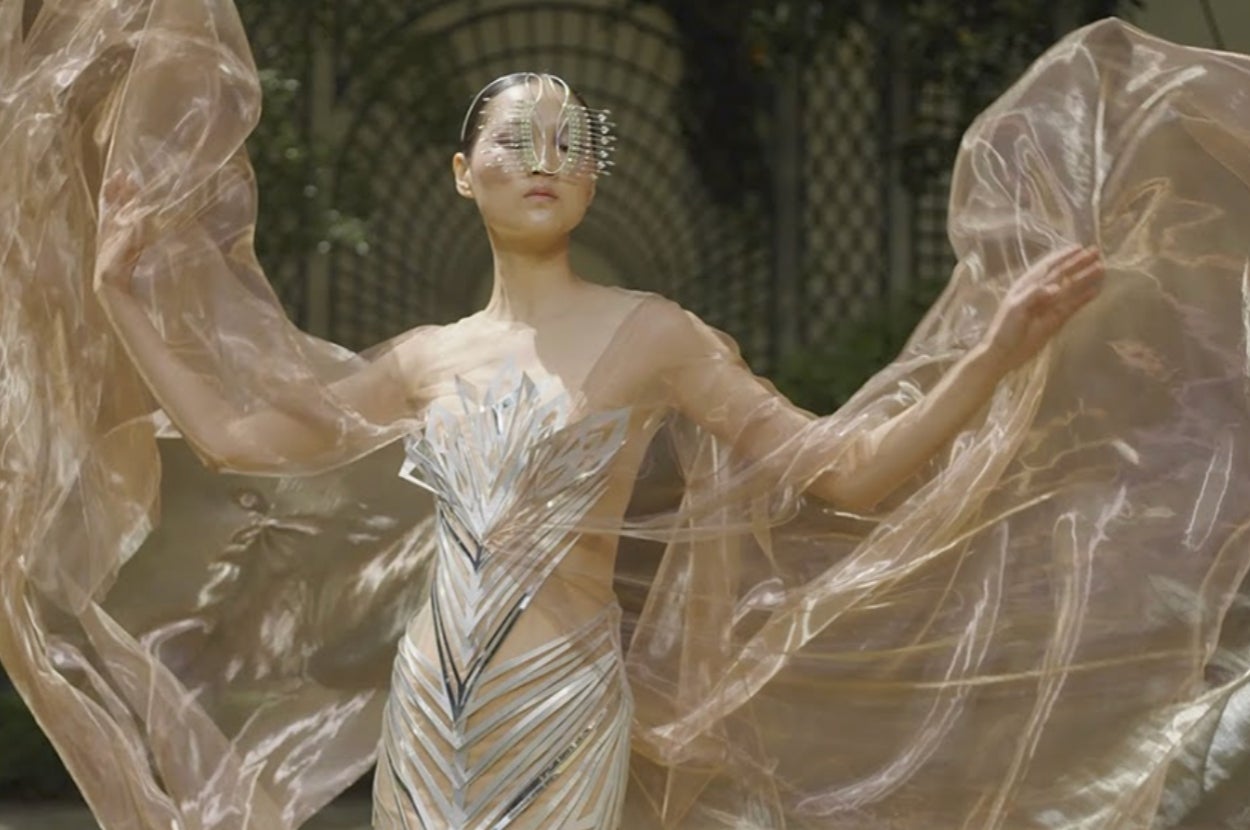 Person wearing a futuristic, structured gown with metallic accents, featuring sculptural wing-like extensions