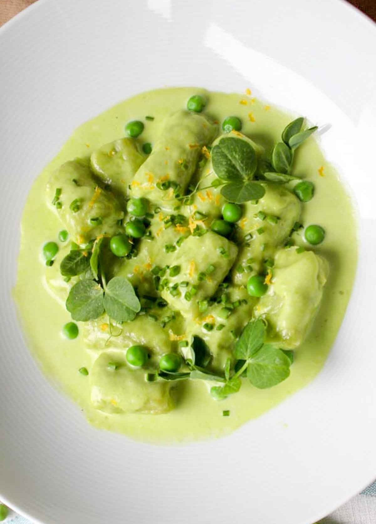 A achromatic  sheet  of gnocchi successful  creamy greenish  sauce, garnished with peas and herbs, presented successful  a gourmet style
