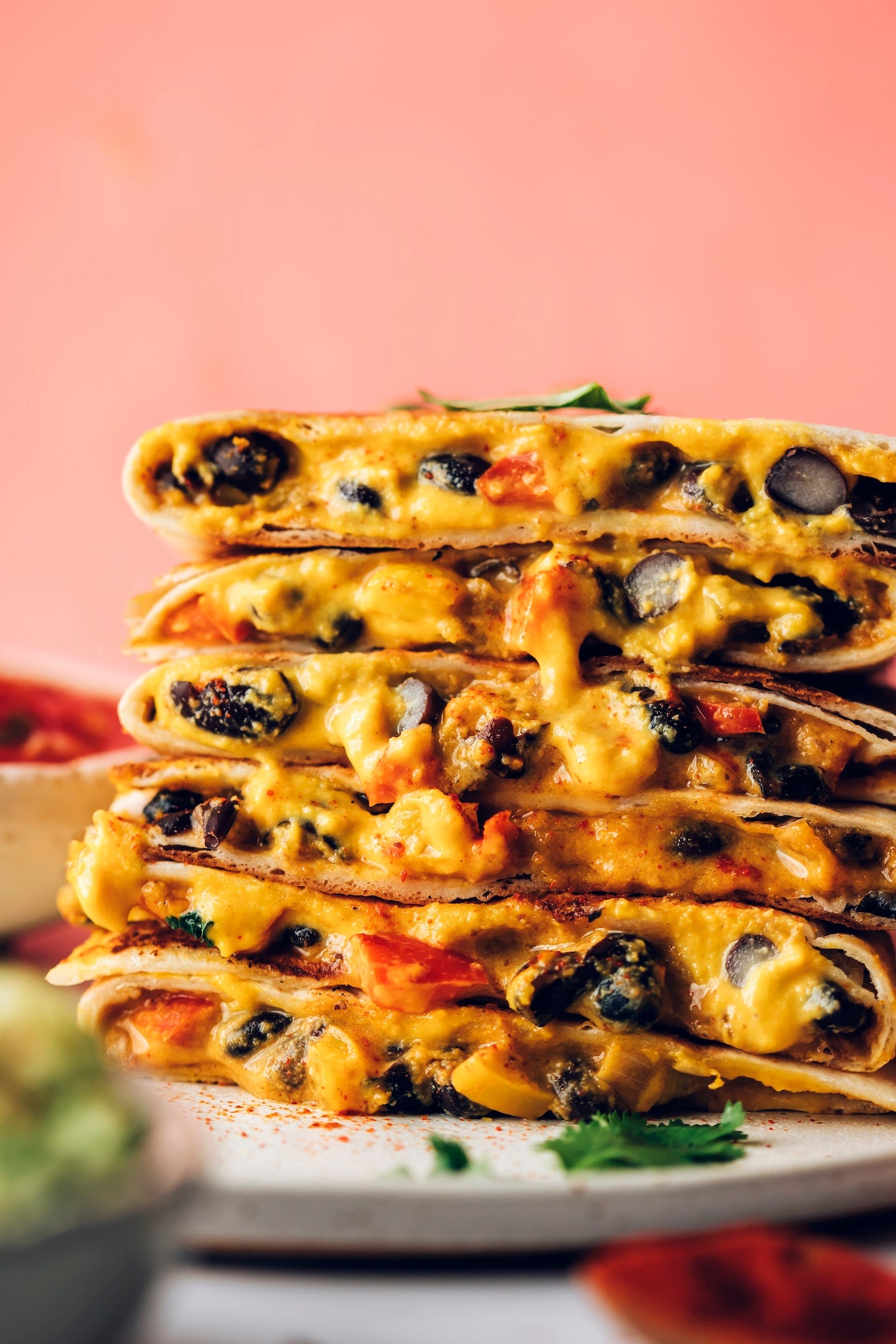 Stack of cheesy quesadillas filled with vegetables and beans, served with dips on the side