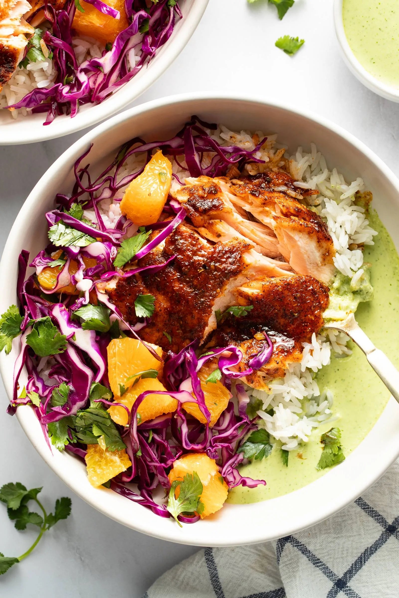 Salmon rice bowl with red cabbage, mandarin slices, cilantro, and green sauce drizzled on the side
