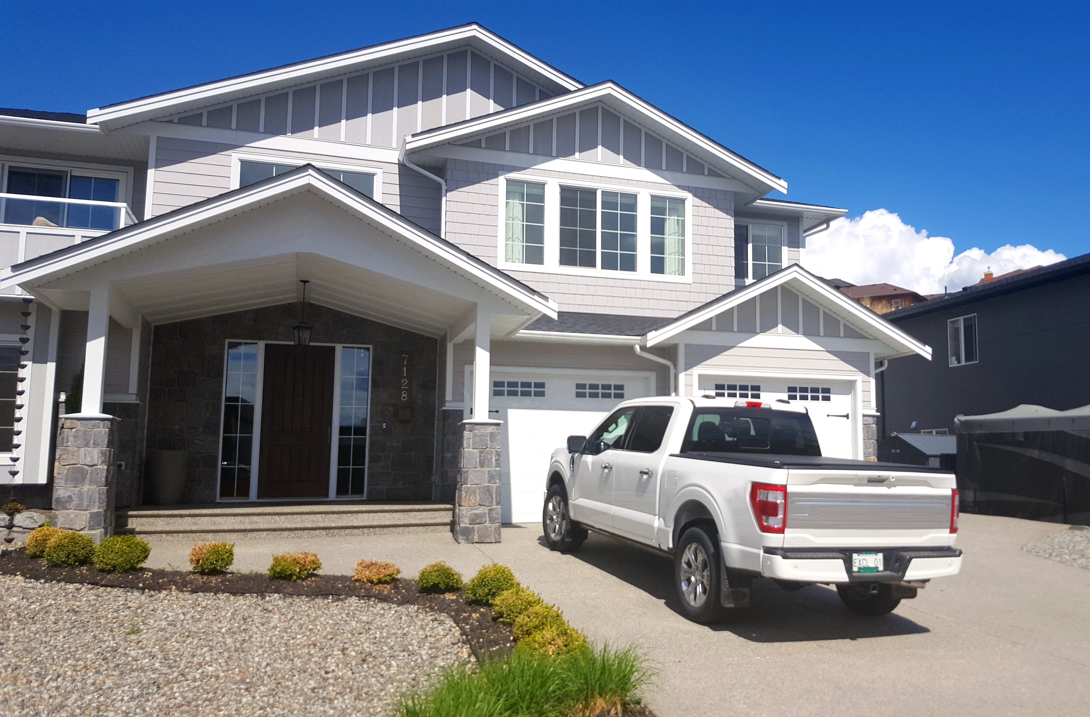 A achromatic  motortruck  parked connected  the driveway of a modern   suburban location   with a chromatic  and wood   facade