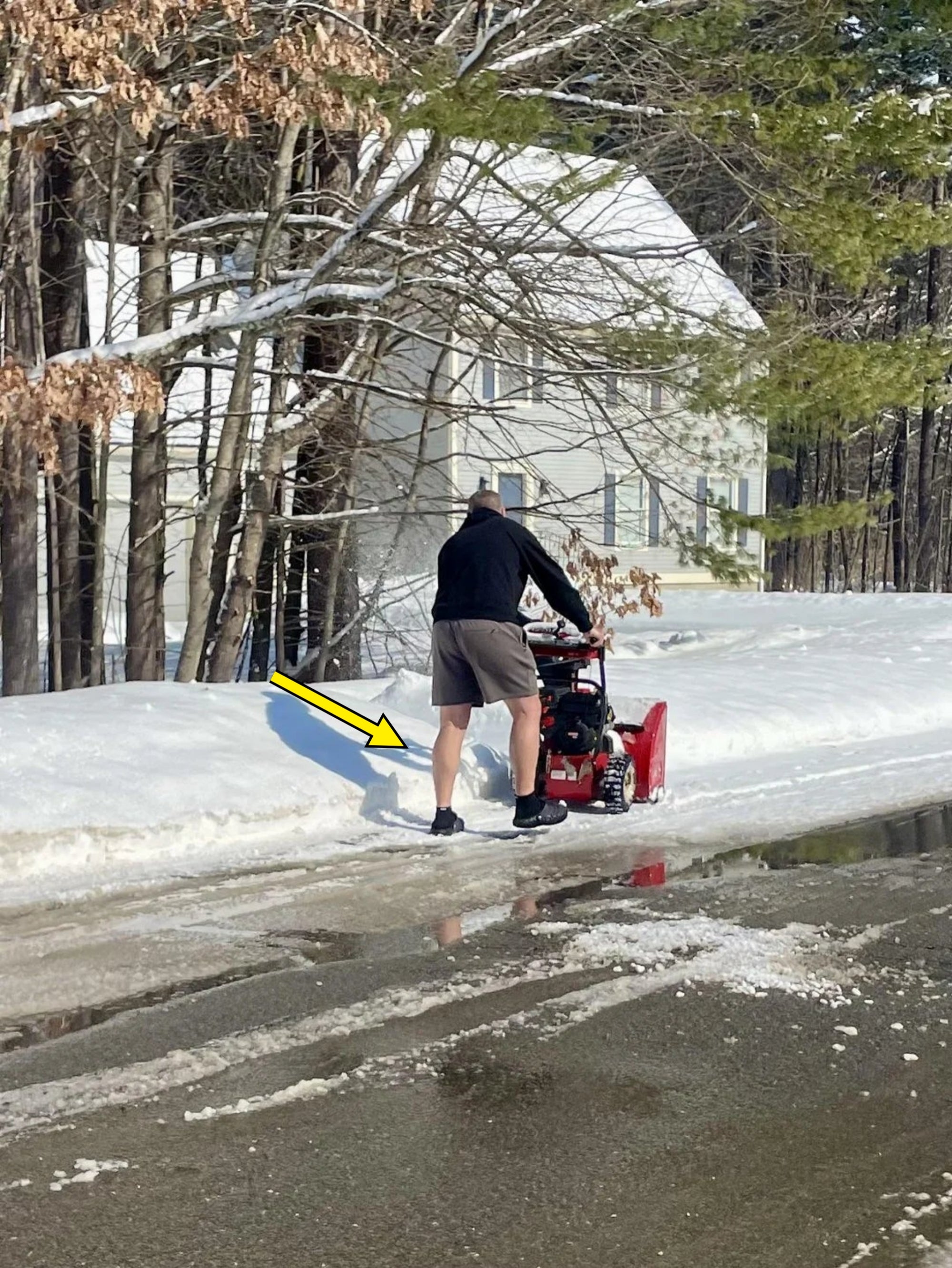 A idiosyncratic   wearing shorts and a hoodie uses a snowfall  blower connected  a snowy way  successful  beforehand   of a house
