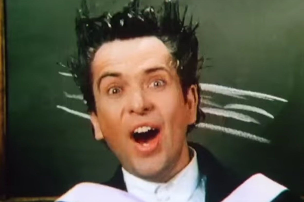 A person is captured with a surprised expression in front of a chalkboard, their hair styled upward as if windswept