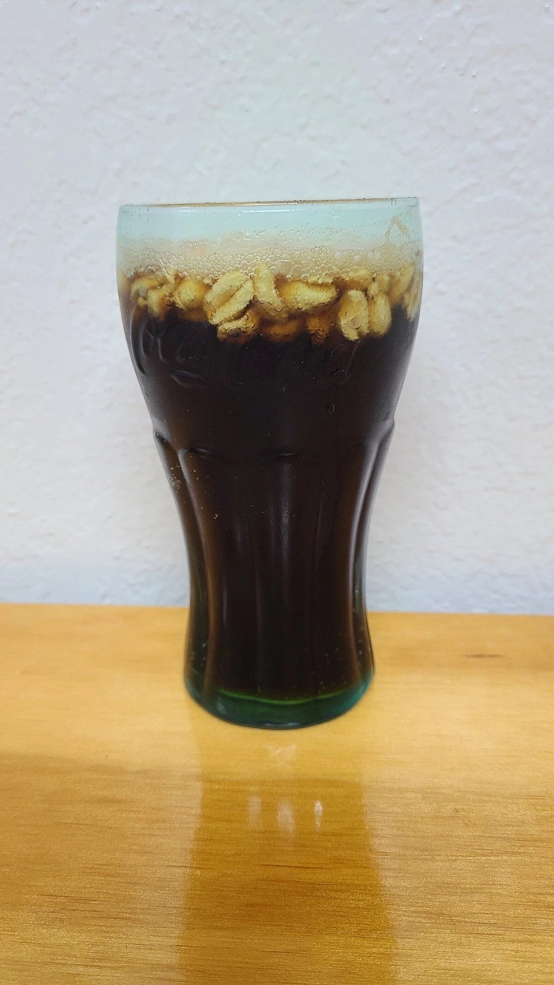 A tall glass filled with a dark beverage topped with oats on a wooden table