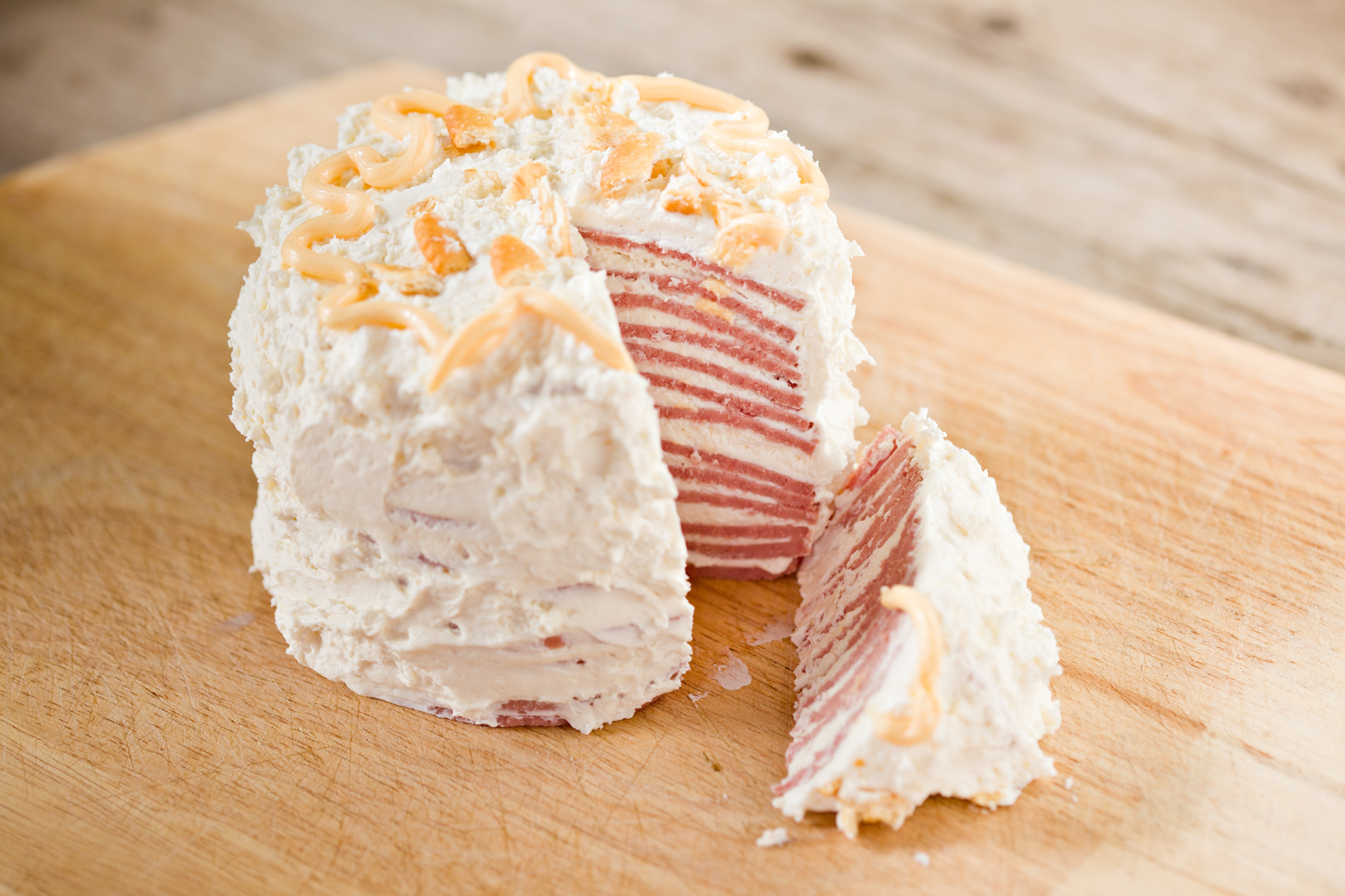 Layered meat cake with creamy frosting on wooden board