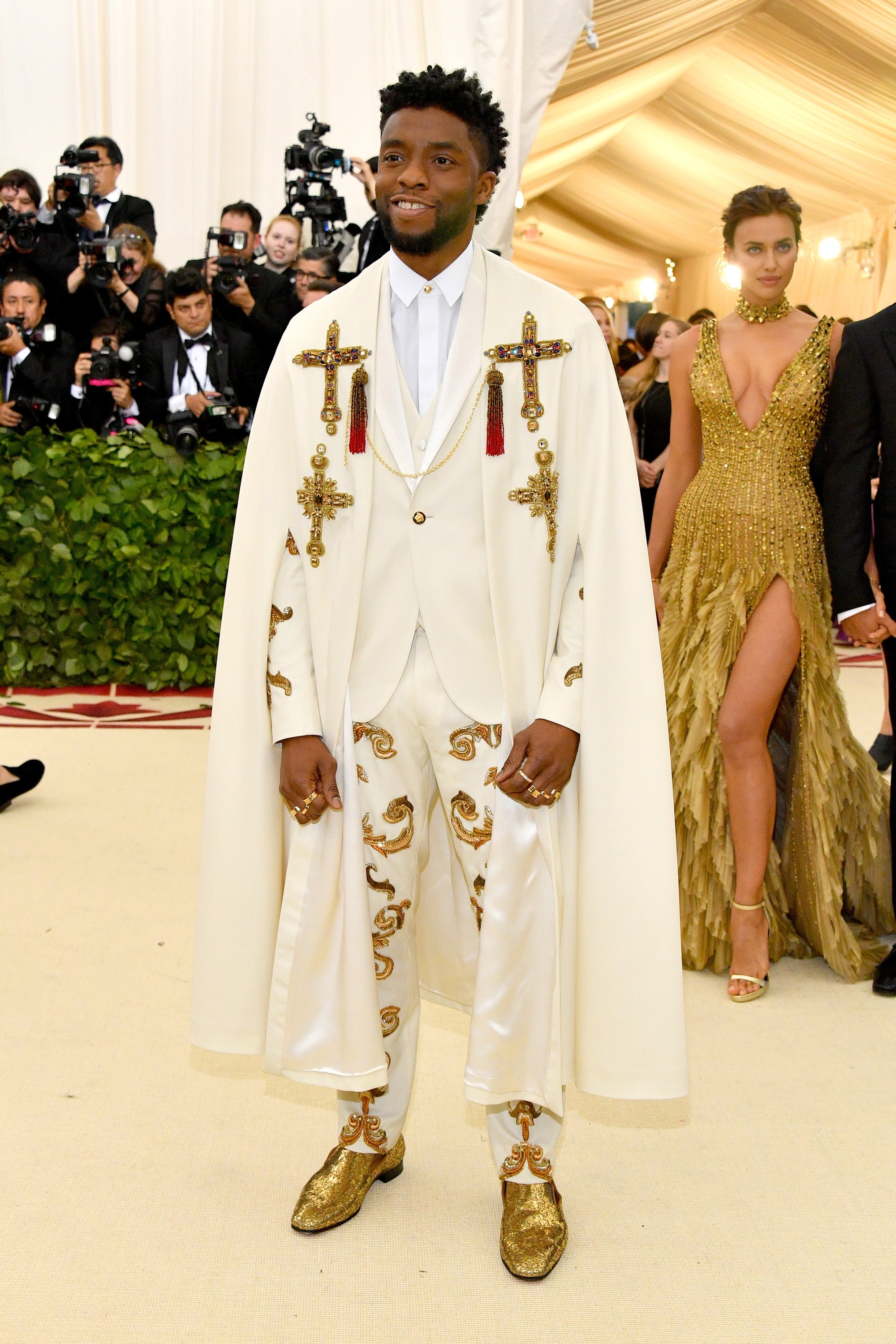 Celebrity successful  an ornate achromatic  suit   with golden  embellishments and cape, posing connected  the reddish  carpet arsenic  photographers seizure  the moment