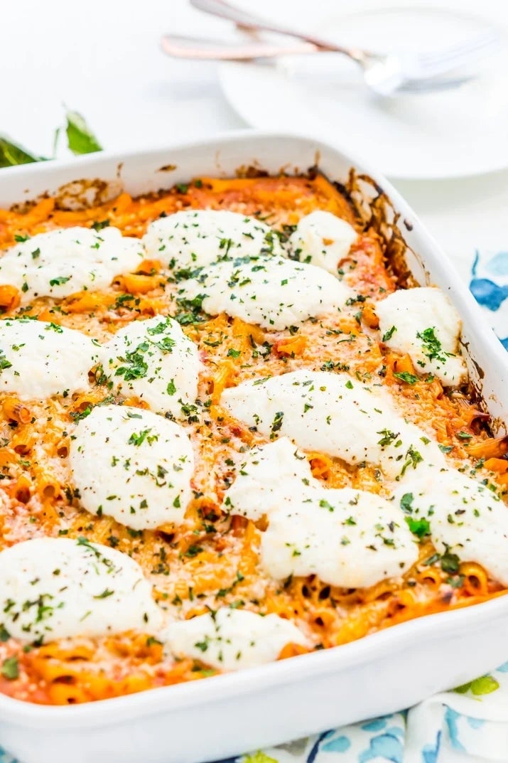 Baked ziti in a casserole dish topped with melted cheese and herbs, ready to serve with a fork on a nearby plate